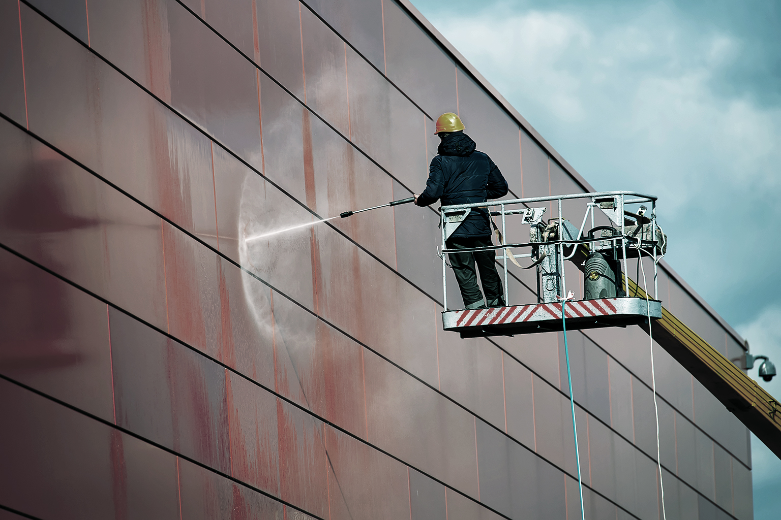 Worker wearing safety harness washes wall facade at height