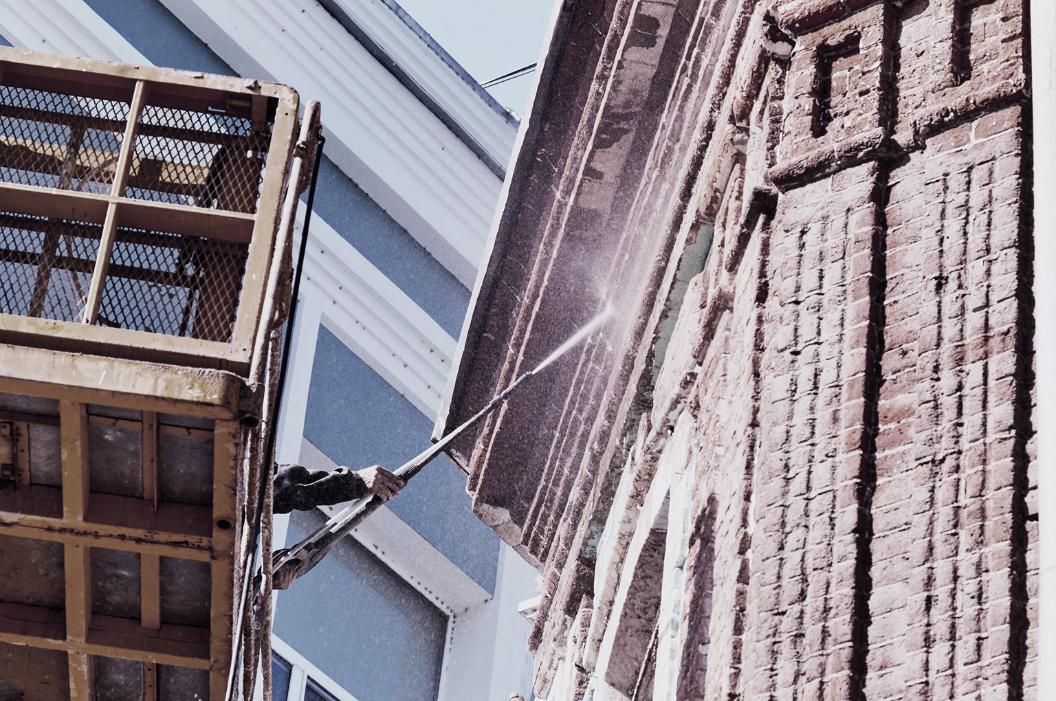Water jet cleaning of facades. High pressure washing of the facade of a historic building using a hydraulic lift. A worker directs a jet of water at a red brick surface. Splash cloud.