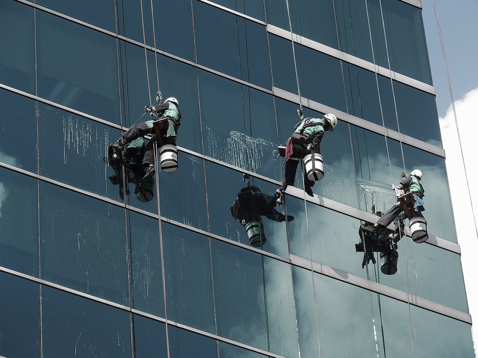 men cleaning glass building by rope access at height